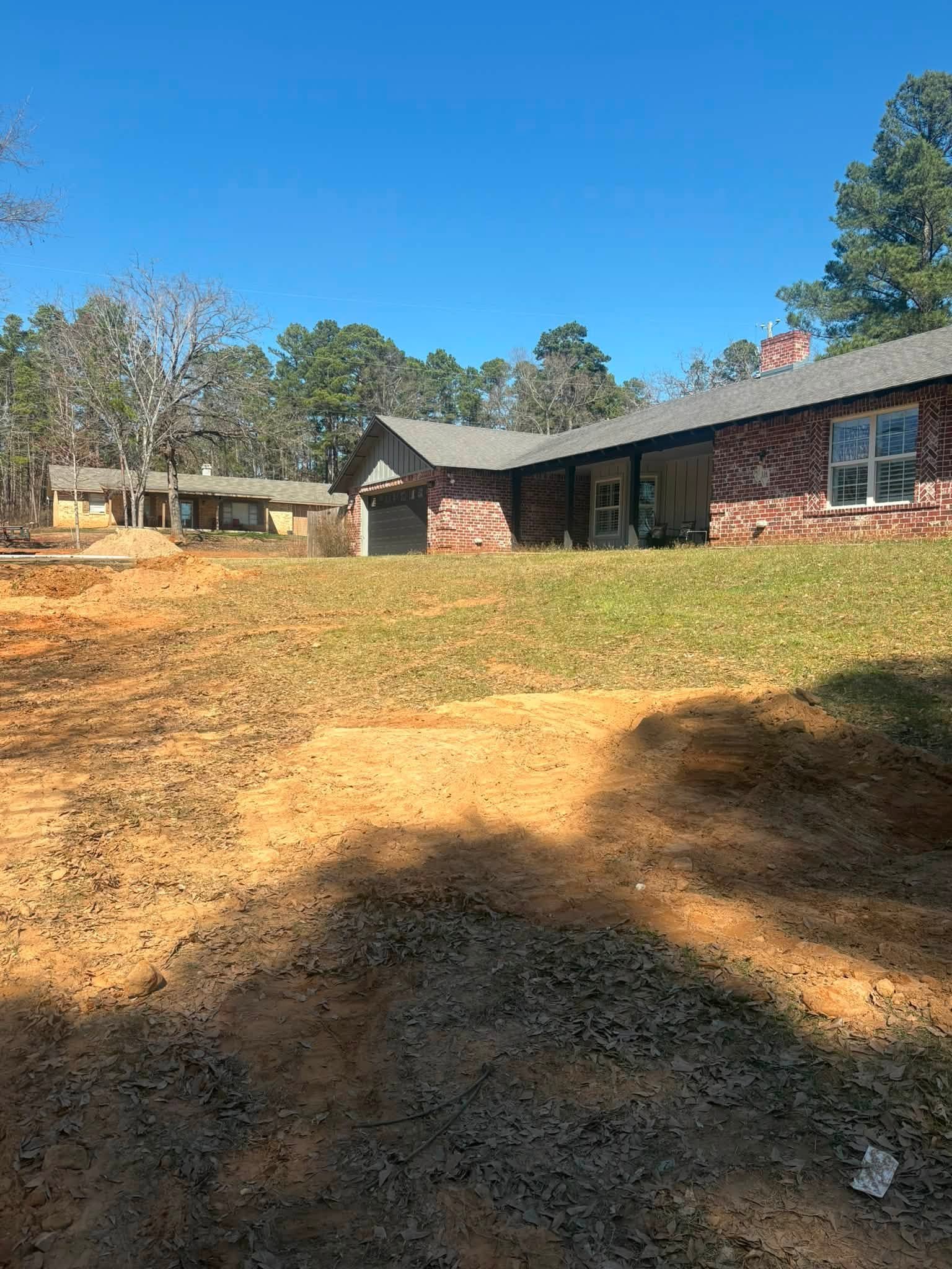 Residential yard with grass and exposed soil beside a brick house